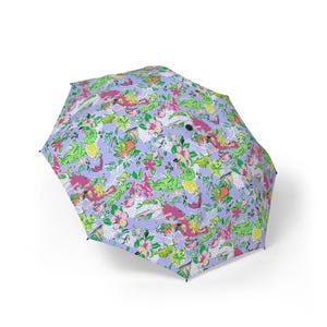 May include: A lilac umbrella featuring a lively pattern of green alligators, pink flowers, and tropical fruits. The design incorporates white and light blue geometric shapes. The umbrella is open, displaying its full, colourful design.