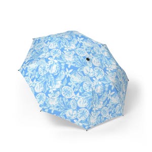 May include: A light blue umbrella featuring a white citrus fruit and floral design. The open umbrella displays a pattern of lemons, oranges, and leaves. A fashionable accessory for sun or rain, with a diameter of approximately 90 cm.