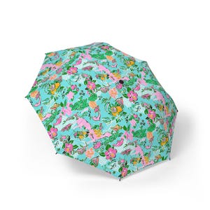 May include: A fully open umbrella displaying a colourful floral pattern. The design incorporates pink, yellow, and green flowers, alongside other tropical motifs, on a light blue backdrop. The umbrella is open, highlighting its bright and cheerful design.