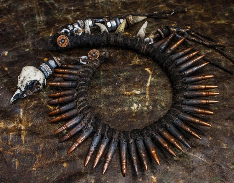 Op de afbeelding: Een ketting gemaakt van kogelhulzen, gewikkeld in donkerbruin touw, met een schedelhanger en andere metalen accenten.