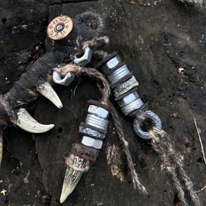 Op de afbeelding: Twee handgemaakte wapenachtige voorwerpen met beenachtige handvatten, omwikkeld met touw en versierd met metalen moeren en een geweerschot. De voorwerpen liggen op een donker houten oppervlak.