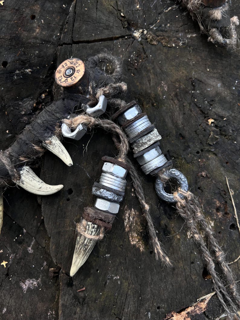 Op de afbeelding: Twee handgemaakte wapenachtige voorwerpen met beenachtige handvatten, omwikkeld met touw en versierd met metalen moeren en een geweerschot. De voorwerpen liggen op een donker houten oppervlak.