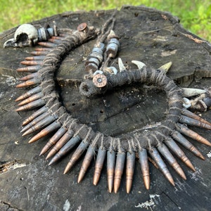 Puede incluir: Un collar hecho de casquillos de bala, cuerda y hueso. El collar es marrón y plateado y tiene un aspecto rústico.