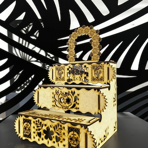 May include: A three-tiered wooden display stand with intricate laser-cut Day of the Dead-themed designs. The stand features a scalloped edge and a floral arch handle. The designs include skulls, flowers, and decorative patterns. The stand is made of light-colored wood.