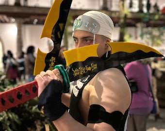 Puede incluir: Un accesorio de cosplay con una gran hoja curva, amarilla y negra. El mango es rojo con un agarre negro. La hoja tiene caracteres japoneses. La persona lleva un pañuelo blanco y brazaletes negros.