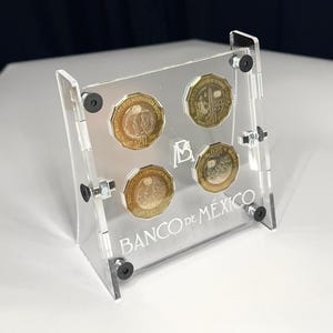 以下が含まれることがあります： 金と銀の色調のメキシコ20ペソ硬貨4枚を保持する透明なアクリル製ディスプレイスタンド。スタンドには黒い金具、中央のロゴ、および前面下部パネルに白で印刷されたBANCO DE MÉXICOのテキストが特徴です。