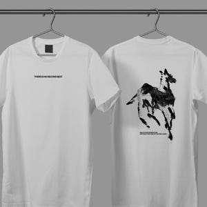 May include: Two white t-shirts hanging on a rail. The front of the shirt has the text "THERE IS NO SECOND BEST". The back of the shirt features a black and white horse illustration with text. The shirts are made of a soft material.