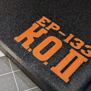 May include: Close-up of a black, textured surface with the orange text "EP-133 K.O. II" printed on it. The text is in a bold, sans-serif font. The surface appears to be a pad or a case.