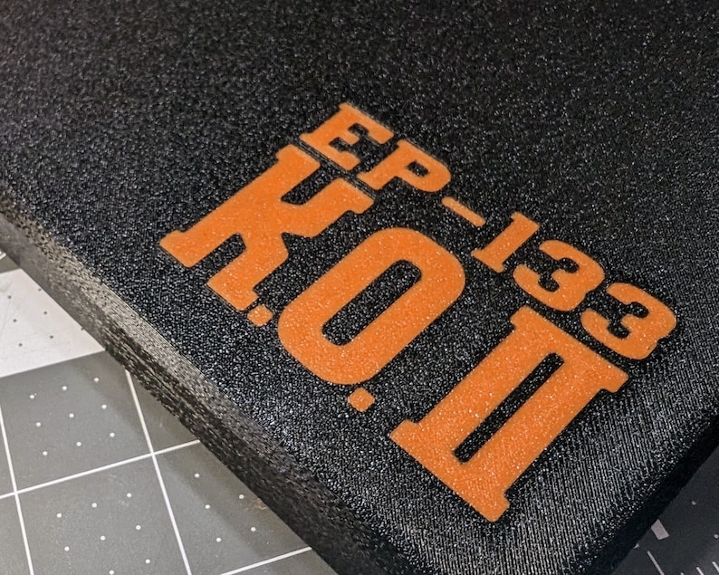 May include: Close-up of a black, textured surface with the orange text "EP-133 K.O. II" printed on it. The text is in a bold, sans-serif font. The surface appears to be a pad or a case.