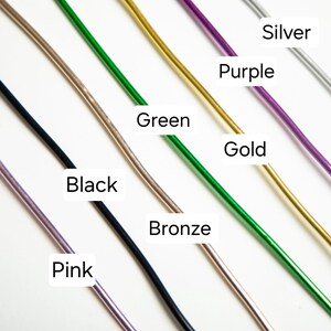 May include: A close-up of seven different colored wires, including pink, black, bronze, green, gold, purple, and silver. The wires are arranged in a diagonal line from the top left to the bottom right of the image.