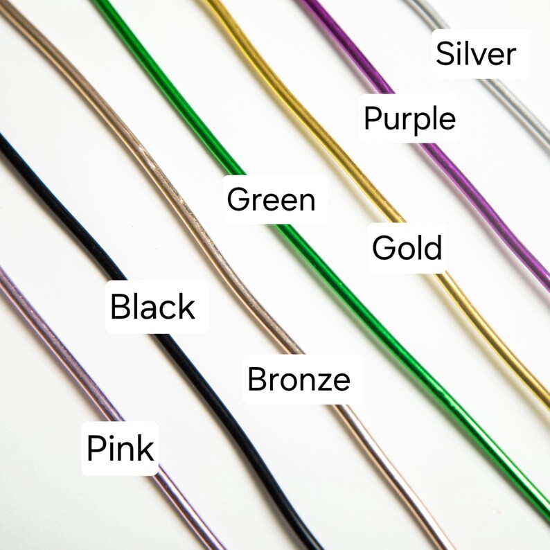 May include: A close-up of seven different colored wires, including pink, black, bronze, green, gold, purple, and silver. The wires are arranged in a diagonal line from the top left to the bottom right of the image.