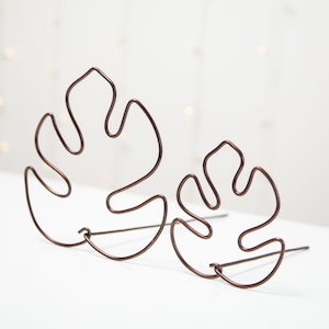 Peut inclure: Deux sculptures de feuilles de monstera en fil de cuivre. Les feuilles sont reliées à la base et se tiennent debout.