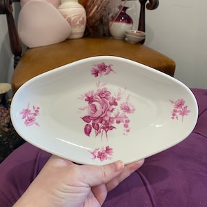 May include: A white oval dish with a pink floral design. The dish has a raised rim and a scalloped edge.