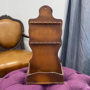 May include: A wooden wall-mounted organizer with a small shelf and multiple pegs for hanging items. The organizer is stained a dark brown color and has a rustic, farmhouse style.