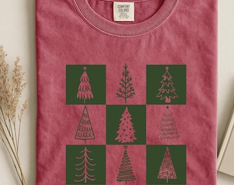 May include: A red t-shirt with a crew neck featuring a grid of nine green squares, each containing a unique Christmas tree design. The shirt has a Comfort Colors tag.