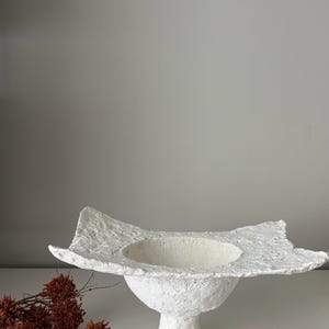 May include: A white ceramic mug with a black handle and the text "But First, Coffee" in a black, bold font. The mug is sitting on a wooden surface. The mug is approximately 4 inches tall.