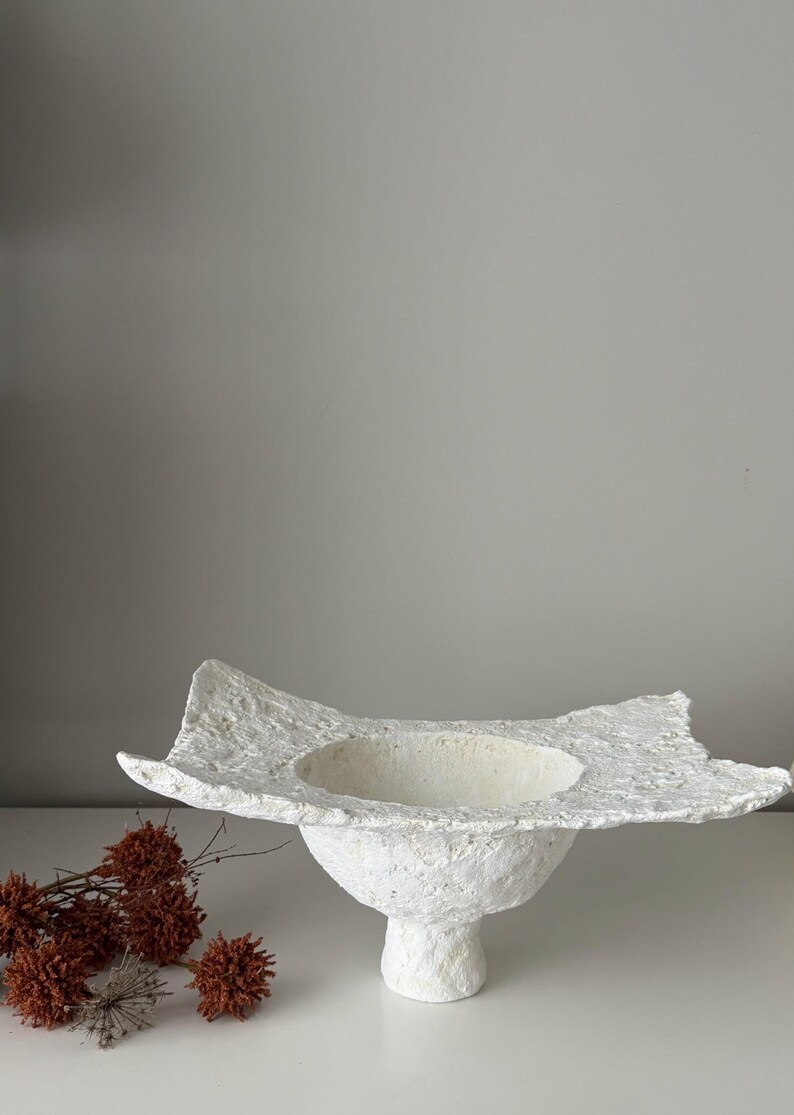 May include: A white ceramic mug with a black handle and the text "But First, Coffee" in a black, bold font. The mug is sitting on a wooden surface. The mug is approximately 4 inches tall.