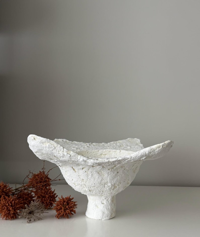 May include: A white ceramic mug with a black handle and the text "But First, Coffee" in a bold, black font. The mug is set against a neutral background, highlighting its simple design.