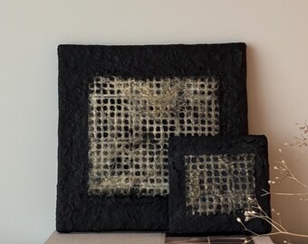 May include: Two black framed wall art pieces with a woven texture in the center. The larger piece is on top of a book titled "Soft Minimal".