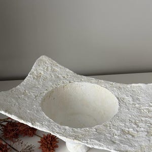 May include: A set of three ceramic mugs with a speckled, matte finish. The mugs are in shades of cream, light brown, and dark brown. Each mug has a simple, minimalist design and a rounded handle.