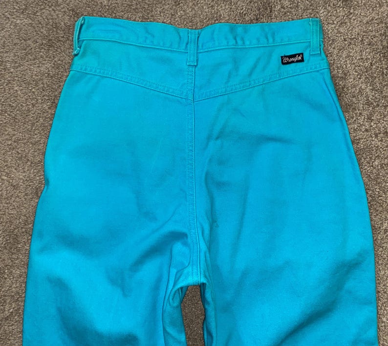 May include: A pair of high-waisted blue denim trousers with a Wrangler label on the back pocket.