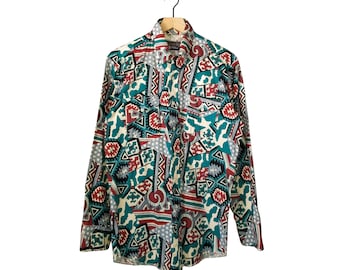 May include: A long-sleeved button-down shirt with a colorful geometric pattern in teal, red, gray, and white. The shirt is hanging on a wooden hanger against a white background. The pattern includes shapes like triangles, stars, and abstract designs.
