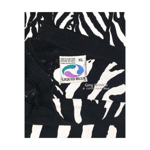 May include: Black XL t-shirt with a white zebra stripe pattern. The tag reads "100% Cotton Made in USA" and "Liquid Blue". The shirt is from 1993 and designed by Greg Genrich.