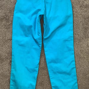 May include: A pair of turquoise blue trousers with a Wrangler label on the back right pocket.