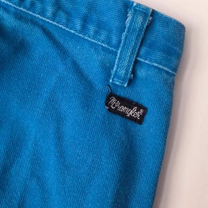 May include: Close-up of a section of bright turquoise denim jeans. The jeans feature a belt loop and a black rectangular tag with the brand name "Wrangler" in white script. The fabric has a textured appearance.