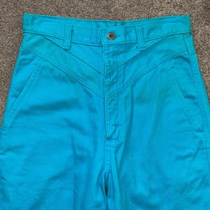 May include: A pair of high-waisted turquoise blue jeans with a unique Y-shaped seam detail on the front.