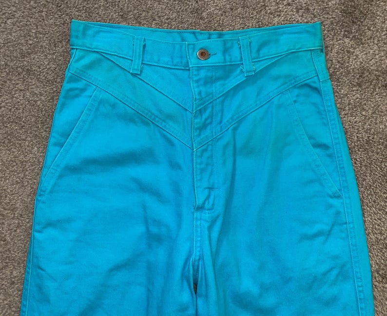 May include: A pair of high-waisted turquoise blue jeans with a unique Y-shaped seam detail on the front.