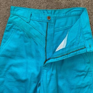 May include: A pair of turquoise blue high-waisted trousers with a zip fly and a button fastening.