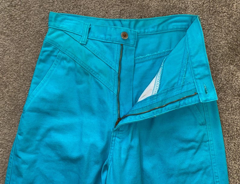 May include: A pair of turquoise blue high-waisted trousers with a zip fly and a button fastening.