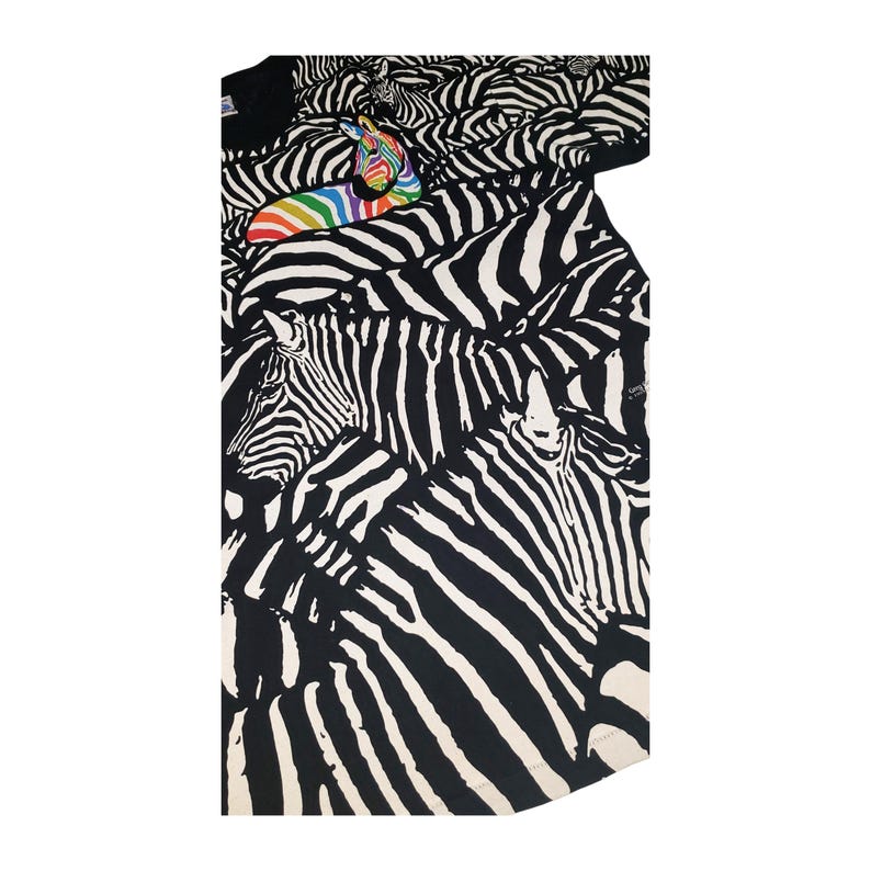 May include: Black and white zebra print t-shirt with a rainbow zebra figure on top. The shirt features a repeating pattern of zebra heads and stripes. The t-shirt is made of a soft material.