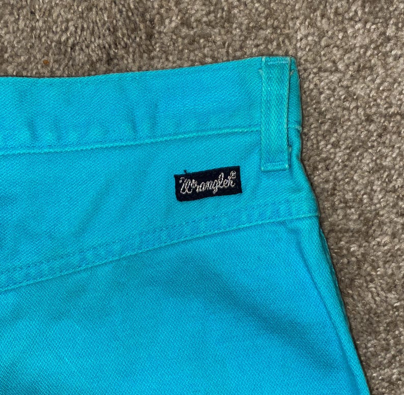 May include: A pair of turquoise blue denim jeans with a Wrangler logo on the back pocket.