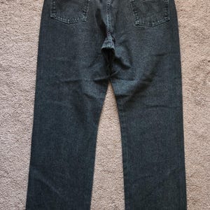 以下が含まれることがあります： クラシックな5ポケットデザインの濃いウォッシュデニムジーンズ。ジーンズは、バックポケットにWranglerブランドのパッチとストレートレッグカットが特徴です。ジーンズはミディアムダークブルーです。