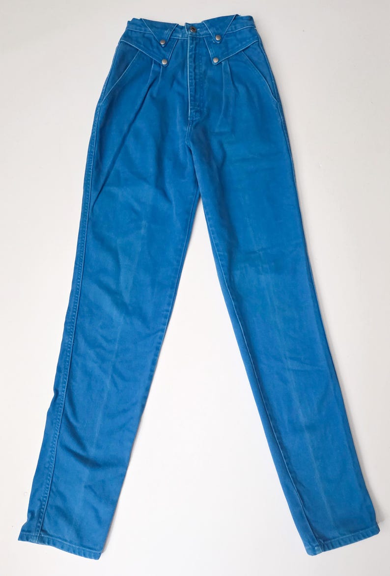 May include: Bright blue high-waisted pants with a button-fly closure and decorative metal buttons. The pants have a classic straight-leg cut and feature front pleats. A vintage style garment.