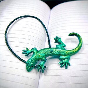May include: A green and blue lizard-shaped bookmark with a black beaded chain.