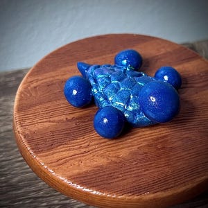 May include: A blue and iridescent resin turtle figurine with five round blue spheres attached to its shell. The turtle is sitting on a wooden surface.