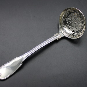 May include: A silver sugar spoon with a decorative, openwork design. The spoon has a long, slender handle and a rounded bowl.