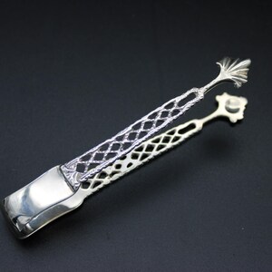 May include: Silver sugar tongs with a decorative openwork design. The tongs have a smooth, rounded handle and a delicate, floral-shaped end.