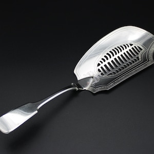 May include: A silver serving spoon with a decorative, openwork design. The spoon has a long, slender handle and a wide, flat bowl with a perforated pattern.
