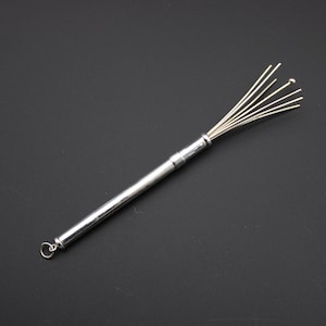 以下が含まれることがあります： 銀色の金属製泡立て器。長く細い円筒形のハンドルが付いており、端には小さな円形のリングが取り付けられています。泡立て器のヘッド部分は、中央のハンドルから放射状に広がる複数の細く真っ直ぐな金属製のワイヤーで構成されています。