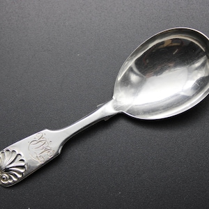 Puede incluir: Una cuchara de plata con un mango adornado y un cuenco redondeado. El mango está grabado con un diseño y las letras "W.S."