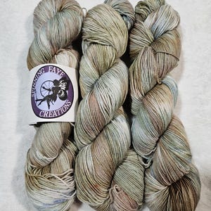 May include: Three skeins of yarn in a variegated colorway of green, brown, and white. The yarn is labeled "Spinning Faye Creations".