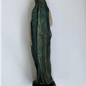 May include: A statue of a robed figure, viewed from the back. The figure is draped in dark green fabric with a textured appearance. The statue rests on a brown, rectangular base. The figure's face is obscured by the hood.