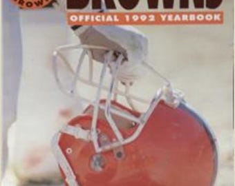 Puede incluir: Un anuario oficial de los Cleveland Browns de 1992 con un casco de fútbol rojo-marrón y una máscara blanca. El nombre del equipo aparece en letras marrones grandes.