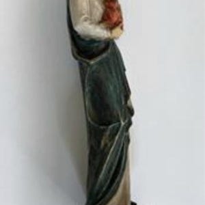 May include: A carved wooden statue of a woman holding a child. The woman wears a white top, a dark green cloak, and a head covering. The child is dressed in red. The statue is mounted on a dark brown wooden base.