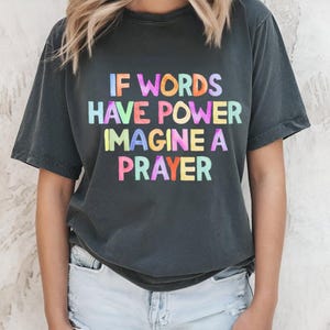 May include: A dark gray t-shirt with the text "IF WORDS HAVE POWER IMAGINE A PRAYER" printed in rainbow colors.