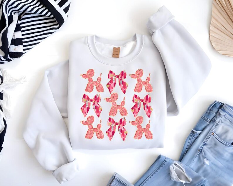 May include: White sweatshirt with a pink and orange graphic print of multiple balloon dogs with bows.